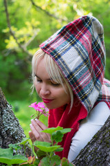 Sweet woman with hood in the forest, smelling the rich aroma of a beautiful pink flower.