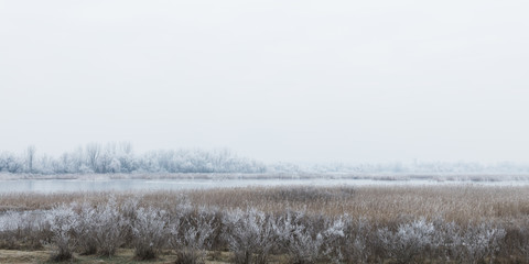 Landscape of frosted fields, river and woods in winter time