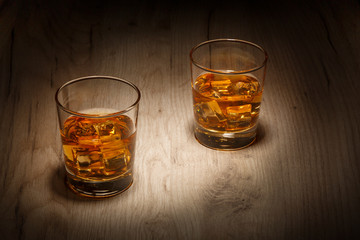 A glass of whiskey with ice cubes on a wooden table. Selective focus.