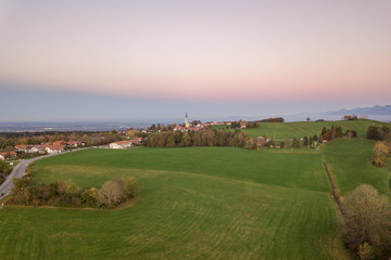 Aerial view of small scattered farm houses with red tiled roofs among green farming fields and...