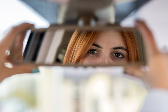 Young Woman Driver Checking Rear View Mirror Looking Backwards While Driving A Car.