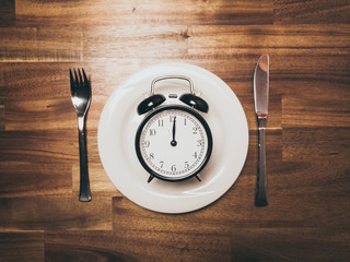 Plate with black vintage Alarm Clock showing Twelve O'clock as symbol for intermittent fasting