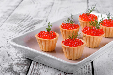 Red caviar served in shortbread tartlets topped with fresh dill on the white ceramic platter