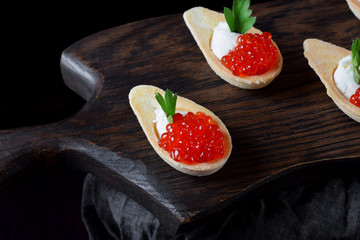 Red caviar and ricotta cheese in the spoon shaped tartlets served on the wooden board