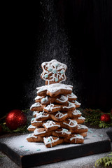 Gingerbread Christmas tree with glazing is sprinkled with sugar powder against the black background