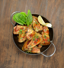 grilled chicken wings with spinach and lime in a bowl on a wooden background
