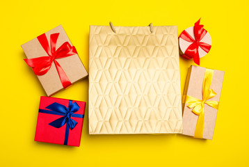 Gold shopping paper bag with gift boxes on yellow background, top view