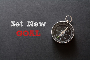 Set New Goal written with Compass on black paper background