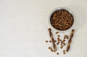 On a white background a metal bowl with dry food and a treat for dogs.