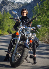 Fototapeta na wymiar A woman in a black leather biker jacket with a carbine rifle on a chopper motorcycle in Greece on a road in the forest in the mountains