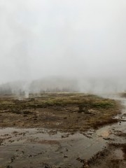 Nordic landscape in Haukadalur valley (Iceland) on a cold autumn / winter day in the geothermal area of The Great Geysir: mud roads, rocks & volcanic nature releasing hot water through geyser springs