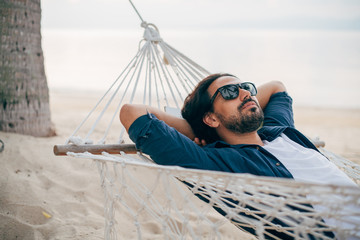 A man enjoys calm, lies in a hammock on the background of the ocean and sunset.