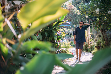 A young man walks in a tropical garden.