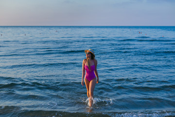 Fototapeta premium Young woman standing by sea. Summer holidays. girl in pink swims
