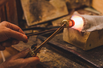 Jeweler at work with a propane burner in a jewelry workshop. Fire close up.
