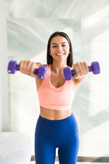 Young pretty woman is exercising with dumbbells at home. Fitness, workout, healthy living and diet concept.