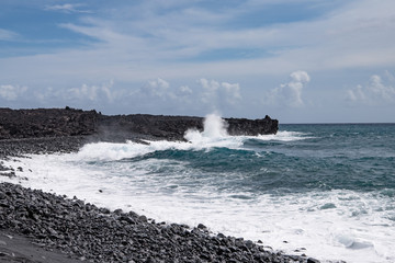 view along coastline with waves on a black sand beach on Hawaii