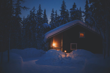 A cozy wooden cabin cottage chalet house covered in snow near ski resort in winter with the lights turn on