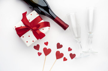 Fototapeta na wymiar composition for holy day Valentine red wine and glasses, gift and hearts made of paper on a white background with copy space for your text