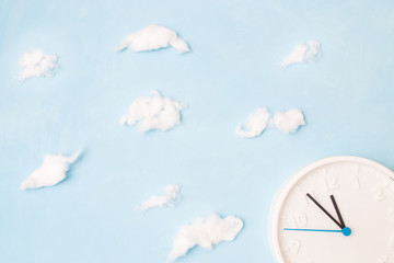 white clock on a blue background with clouds of cotton wool, the concept of time and waste, place copy