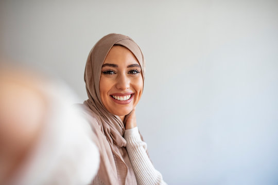 Happy young muslim woman take self portrait with handphone at home. Happy arab woman in hijab with mobile phone making selfie. Portrait of smiling girl, posing.