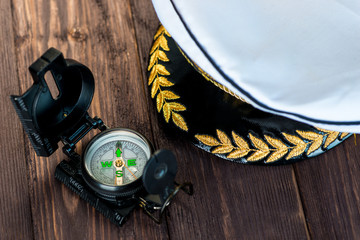 cap of the ship captain and next to it lies a compass on a wooden table