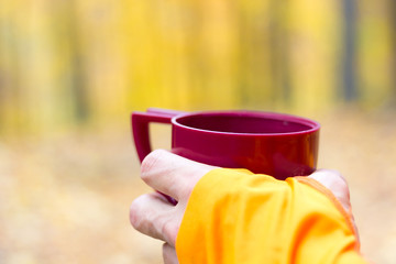 Male runner holding plastic thermos cup at autumn forest backgro