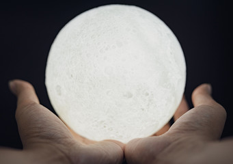 A picture of a hand holding a model of the moon at night
