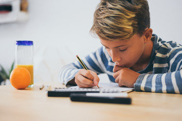 Naklejka premium Student drawing with pencil on the notebook. Boy doing homework writing on a paper. Kid hold a pencil and draw a manga at home. Teen drawing sitting at the table. Education art talent ability concept.