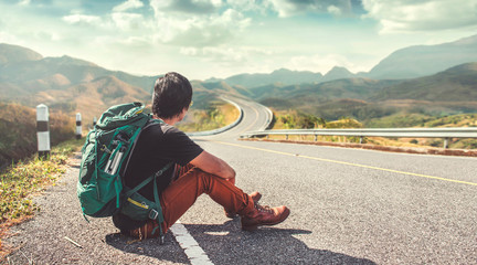 Young man sitting on the roadside. Backpackers, Travel and Holiday concepts.