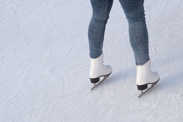 A young woman in white figure skates and blue jeans stands on the ice, ready for the ride on the rink. Training. Winter entertainment and pastime. Leisure and lifestyle. Side view. 