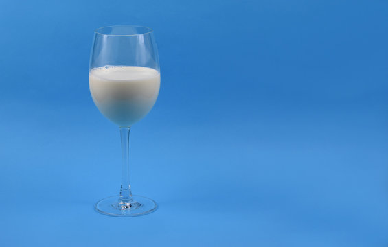 Glass of milk on a blue background stock images. Milk in a wine glass. Wine glass with milk on a blue background. Milk on a blue backdrop with copy space for text