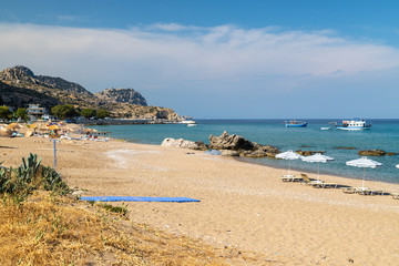 Stegna beach on Greek island Rhodes with sand, sunshades and boats in the background