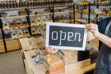 Cropped shot of male owner in apron holding open chalkboard in hands.