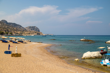 Stegna beach on Greek island Rhodes with sand, sunshades and boats in the background