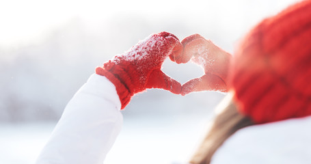 Woman making heart symbol with snowy hands in red gloves, sunny winterday, sun lights, Valentines...