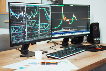 Stock and crypto trading charts on two desktops background on the wood table in office.