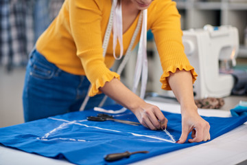 Creative caucasian fashion designer standing in her studio and drawing scheme on blue linen for a beautiful night dress.