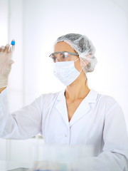 Professional female scientist in protective eyeglasses researching tube with reagents in laboratory. Concepts of medicine and research