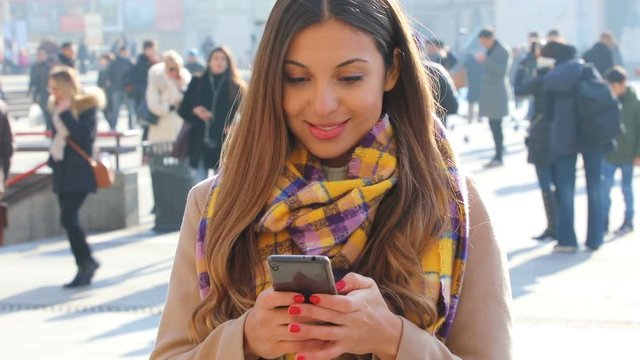 Young woman using instant messaging app on smart phone in Milan city square with blurred crowd of people on the background