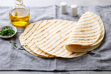 Tortillas, flat breads with olive oil on grey textile background.