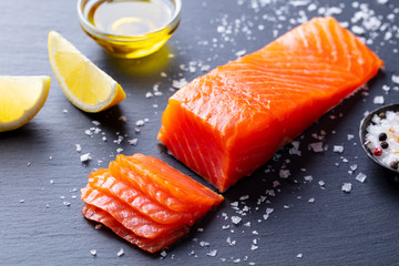 Salmon fillet with sea salt, lemon, olive oil on slate dark background. Close up.