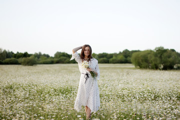 Fototapeta na wymiar Beautiful young woman enjoying a field of daisies, beautiful girl relaxing outdoors, having fun, holding bouquet of daisies, happy young lady and spring-green nature, harmony concept.