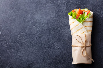 Wrap sandwich, roll with fish salmon and vegetables. Dark background. Copy space. Top view.