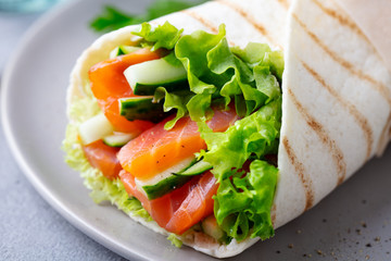 Wrap sandwich, roll with fish salmon and vegetables. Grey background. Close up.