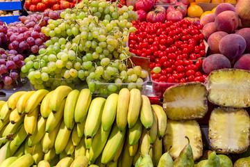Fresh and ripe banana, grapes , peaches, ananas on a fruit counter at the market in Spain. Buy organic food on the local market from rural farms