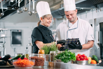 Two chefs discuss the menu in the kitchen of a restaurant or hotel.