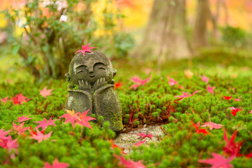 Red Maple leaf on head of Jizo sculpture doll (little Japanese Buddhist monk doll rock) in Japanese Garden.