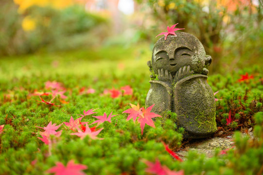 Red Maple leaf on head of Jizo sculpture doll (little Japanese Buddhist monk doll rock) in Japanese Garden.