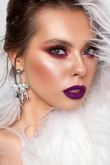 Photo of a very beautiful girl with green eyes, professional purple bright make-up, with earrings from ostrich feathers.